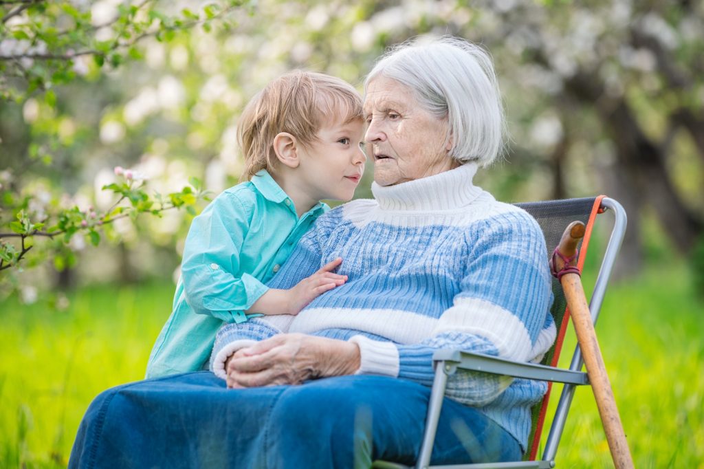 Little boy telling a secret to his great grandmother in a blossoming orchard